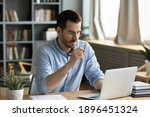 Small photo of Concentrated young businessman in eyewear looking at laptop screen, web surfing information in internet or working distantly online at home office, communication remotely with client or study.