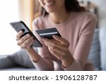 Close up smiling millennial woman holding smartphone and banking credit card, involved in online mobile shopping at home, happy female shopper purchasing goods or services in internet store.