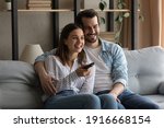 Common interests. Bonding millennial family couple hugging on sofa at living room having pleasure watching movie on tv. Friendly loving young spouses enjoy video film soccer match on weekend evening