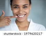 Small photo of Happy African American girl pointing finger at toothy smile, showing healthy white teeth. Client satisfied with dentist service, enamel cleaning, whitening, dental care, orthodontic correction.