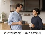 Small photo of Multiracial colleagues talk during lunch break in office kitchen. Indian woman communicates with workmate hold coffee cups enjoy conversation, discuss work or personal. Good relations at work concept