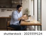Man sit in kitchen wear headphones communicates through videoconference use laptop working remotely from homeoffice. Provide help, explanation and support to client distantly, video call event concept