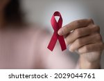 Close up focus on red ribbon in female hands, woman standing indoor promote annual regular health check up, support people with chronic disease, social AIDS campaign, HIV awareness, healthcare concept