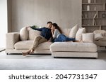 Full length happy relaxed young family couple homeowners or renters lying on big cozy sofa, enjoying carefree leisure weekend time, celebrating moving into new contemporary apartment, tenancy concept.