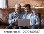 Small photo of Family time with grown son. Elder and younger men relatives sit on sofa at home hug look on laptop screen discuss online news. Retired dad interested in pc talk ask adult child question about app work