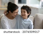 Small photo of Happy cute Indian little son hugging laughing mom, sitting on lap, speaking, telling funny story. Millennial mother holding boy in arms, enjoying leisure with kid, cuddling child. Motherhood concept