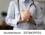 Small photo of Crop close up female doctor physician nurse wearing white uniform with stethoscope holding pink piggy bank, medical insurance concept, healthcare and medicine, hospital budget, clinic fees