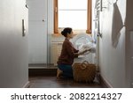 Small photo of Full length tidy young indian ethnic woman folding white laundry clothes bedside towels in modern washing machine, doing household activities in light bathroom, domestic cleaning service concept.