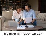 Small photo of Happy couple of tenants, homeowners doing domestic paperwork, reading paper documents, using laptop computer, calculating expenses, paying bills, insurance, mortgage fees on internet with online app