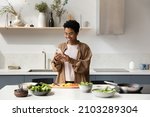 Small photo of Happy Black food blogger girl taking picture of salad ingredients on mobile phones, recording video, shooting cooking process, reading recipe on Internet, chatting online in home kitchen