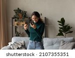 Happy euphoric millennial generation hispanic latin woman looking at mobile phone screen, feeling excited reading message with amazing win news, jumping dancing alone in living room, internet success.