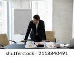 Frustrated concerned business man standing at table with sales reports, paper sticky notes, looking away, thinking over company future, negative statistics result, financial loss