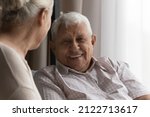 Small photo of Happy elderly 80s man talking to wife, female carer at home, resting on couch, speaking to woman with toothy smile. Later life, old age, elderly care, marriage concept