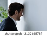 Small photo of Unhappy hysterical young businessman employee manager hitting head against wall, feeling stressed having difficult tasks or problems on work, professional burnout, depression, overworking concept.