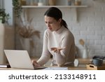 Irritated woman sit at table staring at laptop screen feels angry and confused having problems with broken computer, reading message with bad news in email, lost information, apps malfunction concept