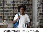 Small photo of Serious teenage African student guy with backpack and workbooks standing in library look at camera. Gaining professional knowledge, get higher education, university studies, newbie in class concept
