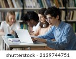 Small photo of Student guy wear glasses studying in library or classroom, using laptop working on essay, prepare for college exams seated at table with diverse group mates. Education, professionals skills concept