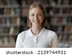 Small photo of Head shot young beautiful teenager girl smile looking at camera. Blond 18s student posing in university library, concept of higher education, high school excellent pupil portrait, studentship concept