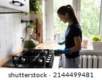Young housewife wear rubber protective gloves standing in cozy kitchen cleans worktop table use rag and effective detergent products. Household, cleaning services, domestic work, housekeeping concept