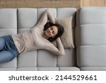 Happy relaxed pretty young woman lying on sofa at home, daydreaming, thinking over good future plans, breathing fresh air, enjoying leisure time, pause, laziness, reloading. Top view