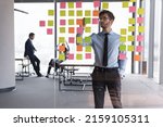 Serious businessman managing project tasks on sticky notes, writes start up business ideas using colorful post it stickers, plan corporate strategy on glass board. Creative priority to-do list concept