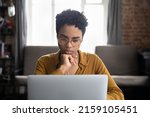Small photo of African woman in glasses sit at desk staring at laptop screen, learn new software, makes assignment, working looks concentrated, search solution or ideas. Business challenge, thinks over task concept