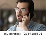 Serious talk. Concentrated young casual businessman in glasses hold smartphone to ear make answer business call contact client. Confident male expert consult customer by phone on professional matter