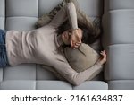 Peaceful pretty 20s girl lying on back on comfortable couch at home, covering eyes with hand, sleeping at daytime, feeling tired, enjoying relaxation, leisure, break, weekend. Top view