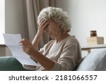 Small photo of Upset elderly woman sitting on couch at home, reading document and getting stressful bad news at home. Frustrated senior lady shocked with letter, touching head, trying to cope with negative emotions