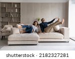 Small photo of Funny excited millennial spouses of new homeowners falling on big soft couch at home. Young couple celebrating moving into first common house. Real estate, renovation, furniture for hoe concept