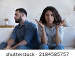 Small photo of Annoyed married couple sitting on couch apart, after conflict, arguing, row. Serious angry wife looking at camera, tired husband turning away. Marriage crisis, counseling, relationships concept