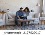 Small photo of Millennial wife and husband sorting out bank papers, check invoices, paying bills via e-bank on laptop sit on sofa smile feel satisfied. Enough money, payments, profit, financial management concept