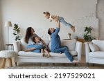 Small photo of Couple with kids gathered in living room play together have fun sit on sofa, loving dad lifts on arms cute daughter, mom with son embracing resting on couch. Well-being family weekend at home concept