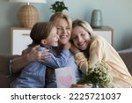 Grandma embrace little granddaughter, thank adult daughter for gift on birthday, holding spring chamomile flowers and postcard, smiling feel happy. Live events, Mothers Day and 8-march celebrations