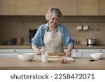 Small photo of Happy senior cook blogger woman baking in home kitchen, rolling dough on floury board, preparing bakery food dessert, smiling, laughing, shooting culinary workshop