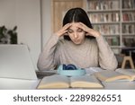 Small photo of Schoolgirl sit at desk with textbook in library cramming, prepare for exams, think, solve math task, read theory, holds her head feels overworked, tired from studying or cramming. Information overload