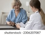 Small photo of GP in white coat talk to patient seated at desk, provide professional consultation to elderly woman, hospital patient, tell about plan of disease treatment, tell for medications during visit in clinic