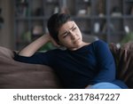 Melancholic mood. Sad depressed young indian woman sit on sofa at home alone think on love work problem cruel life bad health. Upset teenage female suffer from loneliness misunderstanding broken heart