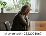 Unhappy old Caucasian woman sit at table at home cry feeling depressed sad suffer from life or health problems. Upset lonely mature female distressed with loneliness solitude, mourn yearn at home.