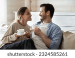 Small photo of Quiet happiness. Happy tender married couple millennial man and woman enjoy being at home together cuddling smiling sitting on sofa at new dwelling having pleasant conversation drinking morning tea