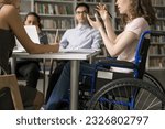 Team of college students and speaker with disability meeting in library, discussing group homework task, class project. Young college girl using wheelchair, talking to classmates. Cropped shot