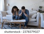 Small photo of Concerned worried married couple getting financial problems, money crisis, counting overspent budget, high mortgage, rental fees, holding heads, looking at paper bills at home