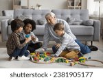 Small photo of Multigenerational family play wooden railway at modern home. Senior great-grandad play railroad with three multiracial boys, siblings, cute great-grandchildren, spend pastime together in living room