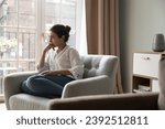 Small photo of Worried young 25s Indian woman sit on armchair looks upset due to life concerns or break up, wait for boyfriend at home feels jealous, thinks over problems, search solution. Personal troubles concept