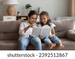Small photo of Indian woman and little girl enjoy fairytale, caring mother reading fascinating book her preschooler daughter spend weekend at home. Pastime and hobby, good life habit, children development concept