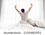 Asian man streching after get up from his bed against white curtains
