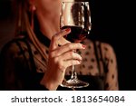 Female hand holding glass of red wine on black background. Woman in  the evening beautiful black blouse