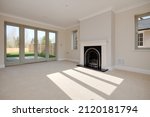 Small photo of Great Wilbraham, Cambridgeshire, England - March 27 2017: Unfurnished living room within brand new home including fireplace and sun casting shadows on the carpet through window
