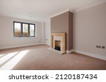 Small photo of Great Wilbraham, Cambridgeshire, England - Feb 24 2017: Unfurnished living room within brand new home including fireplace and sun casting shadows on the carpet through window
