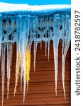 Small photo of Icicles in winter and spring in a selective focus. Roof of the house is covered with ice. Icicles hang from the roof, melting on a bright sunny day. Danger, the falling icicles. Thaw.